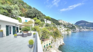 Una propiedad costera con terraza, mobiliario exterior y vista al mar.