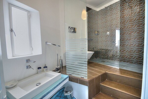 A modern bathroom with a glass shower enclosure, a white sink, and a patterned wall.