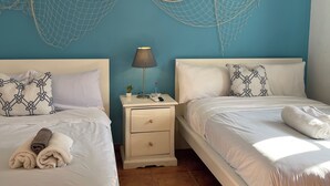 Une chambre avec deux lits, une table de chevet avec une lampe et un ventilateur de plafond.