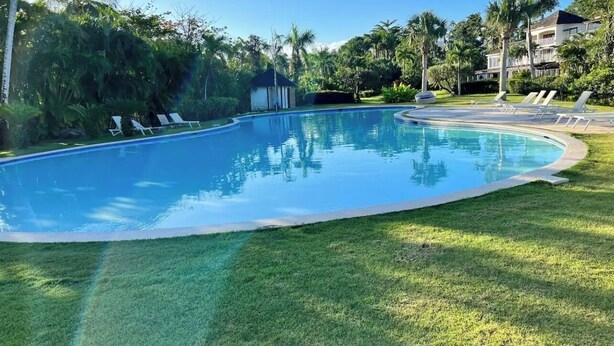 Une piscine d’un bleu éclatant, entourée d’une pelouse bien entretenue et de palmiers.