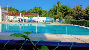 Una piscina con area coperta, un furgone bianco e vegetazione sullo sfondo.