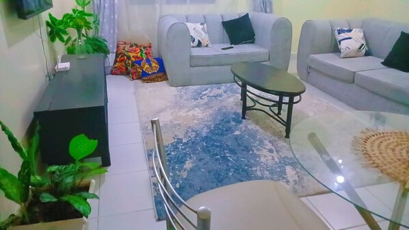 Un salon avec un canapé gris, une table basse en verre et un tapis bleu à motifs.