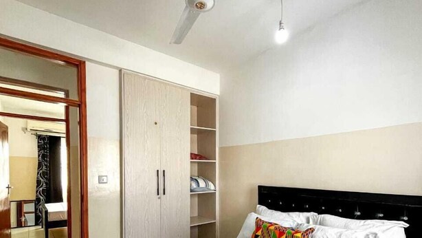 Camera d'albergo con un letto, una ventola a soffitto, un armadio e un bagno visibile tramite una porta aperta.