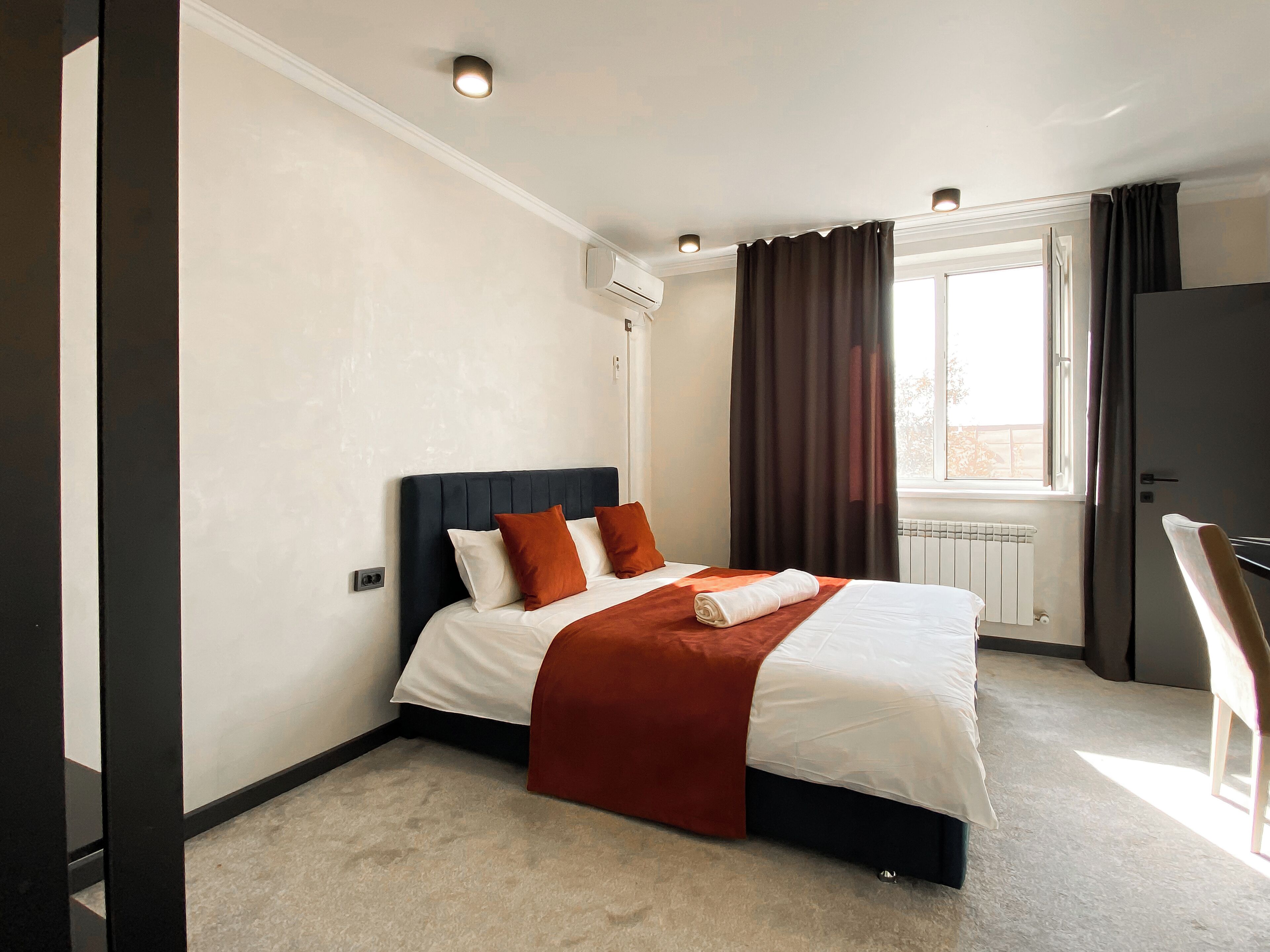 A hotel room with a bed, a window with curtains, an air conditioning unit, and a radiator.