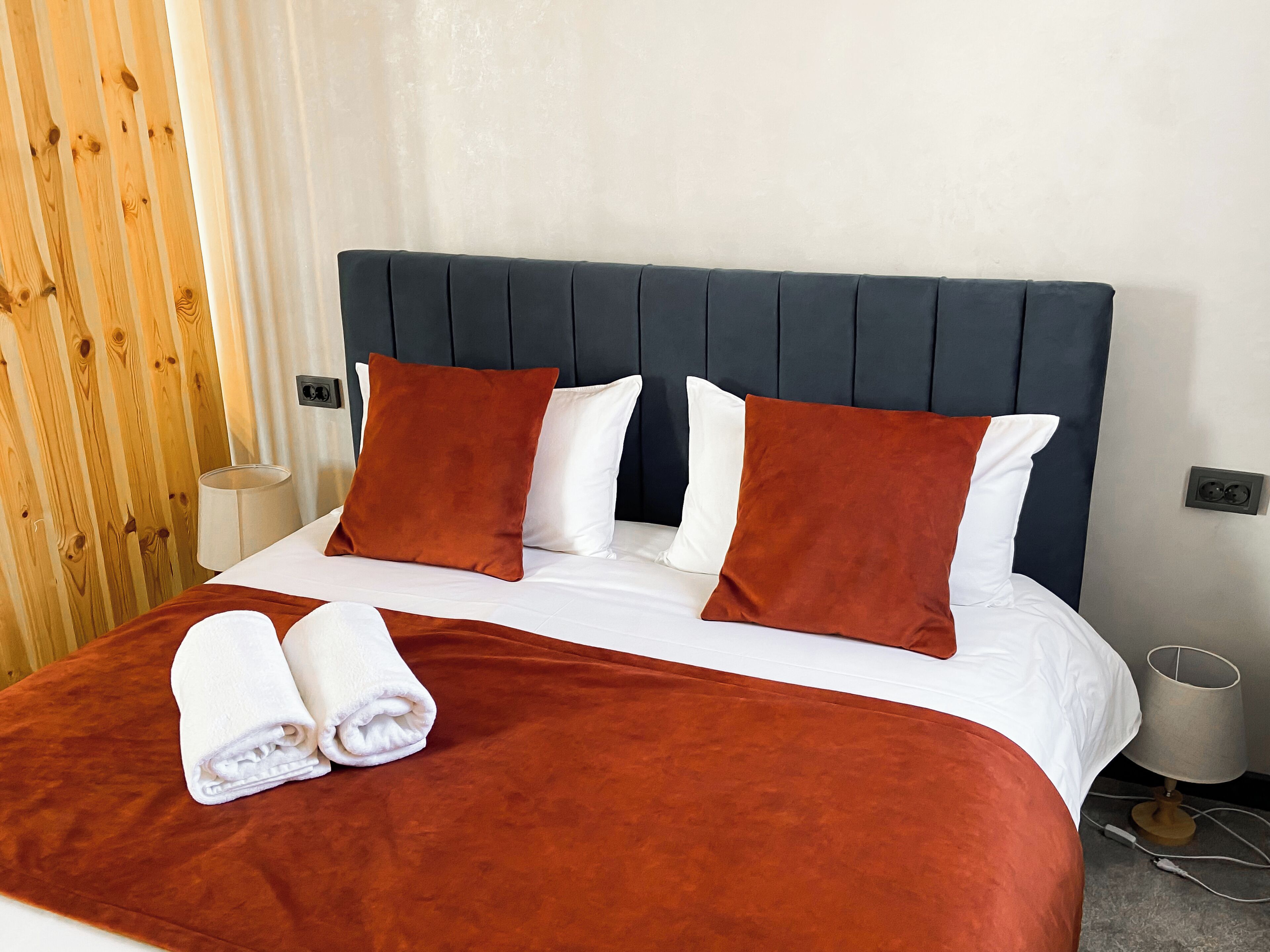 Una cama bien hecha con cabecera oscura, almohadas blancas y marrones, y una colcha marrón.