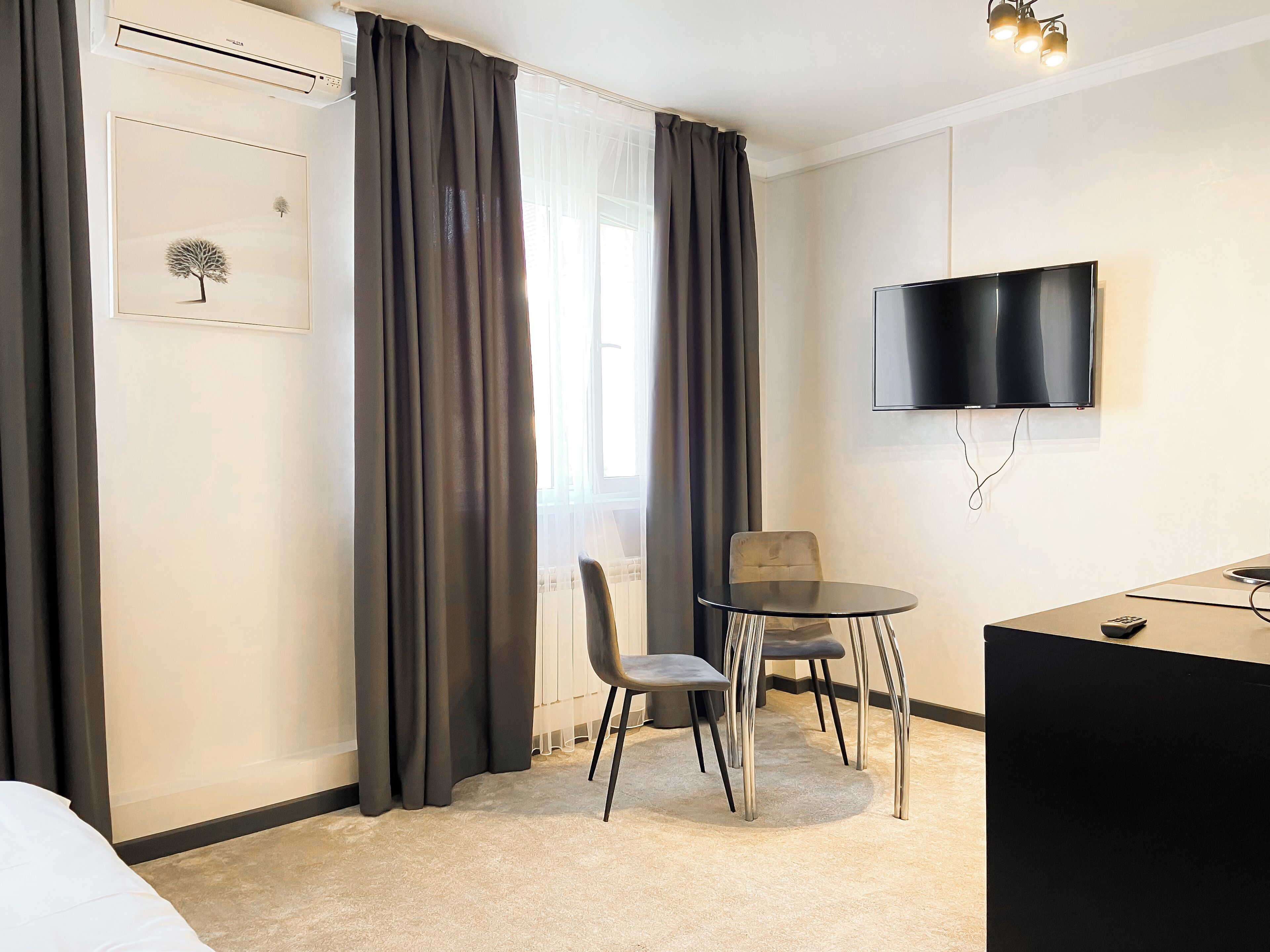 Habitación de hotel con cama, escritorio con silla, televisor montado en la pared y ventana con cortinas.