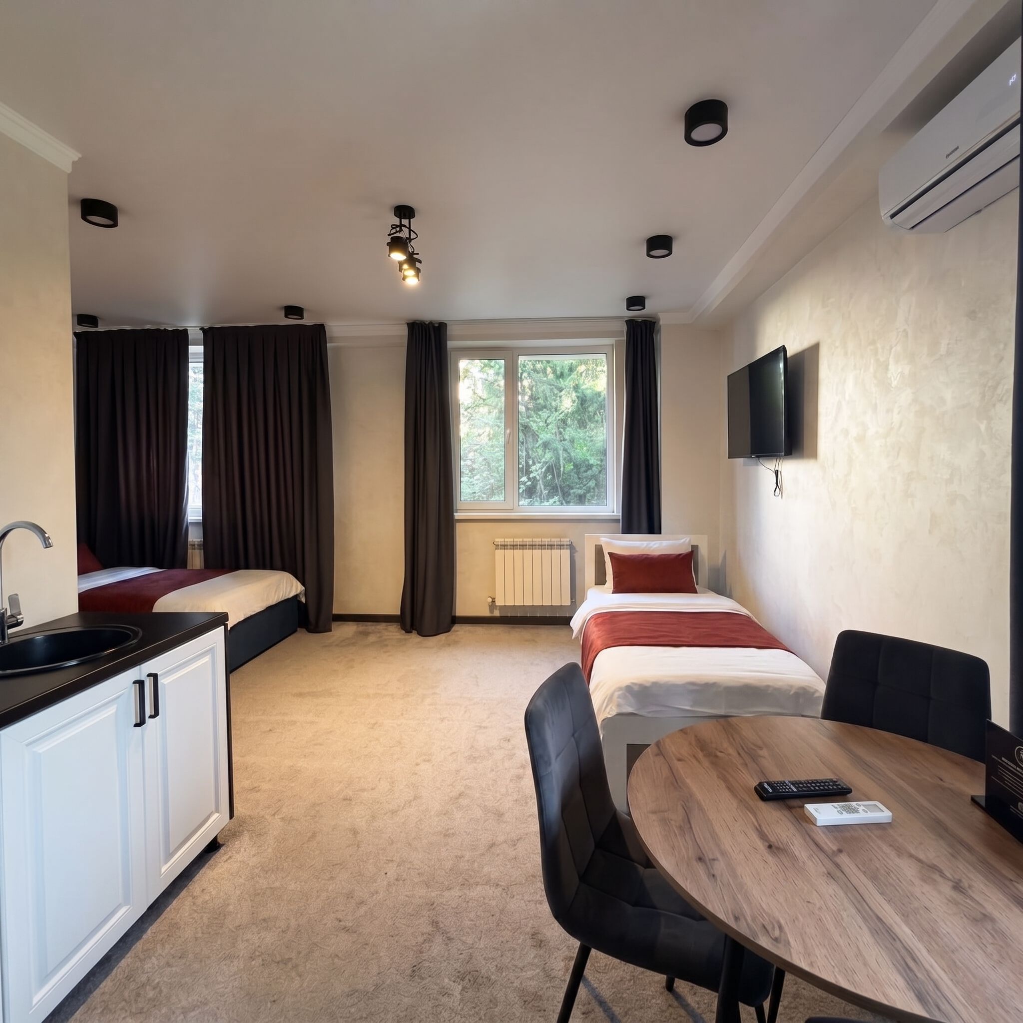 A hotel room with a kitchenette, a bed, a dining table, and a TV.