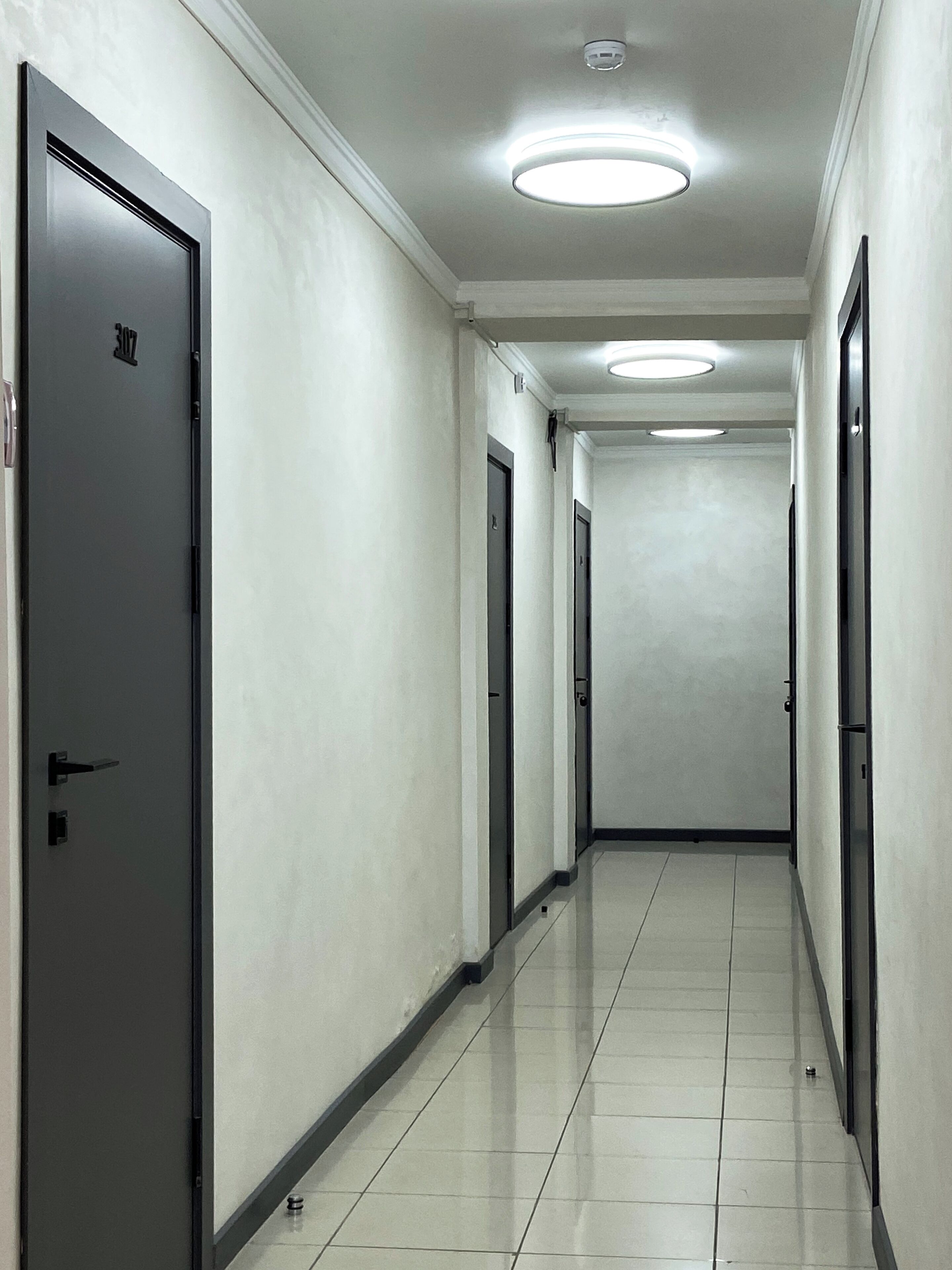 A hallway with doors, a tiled floor, and recessed ceiling lights.