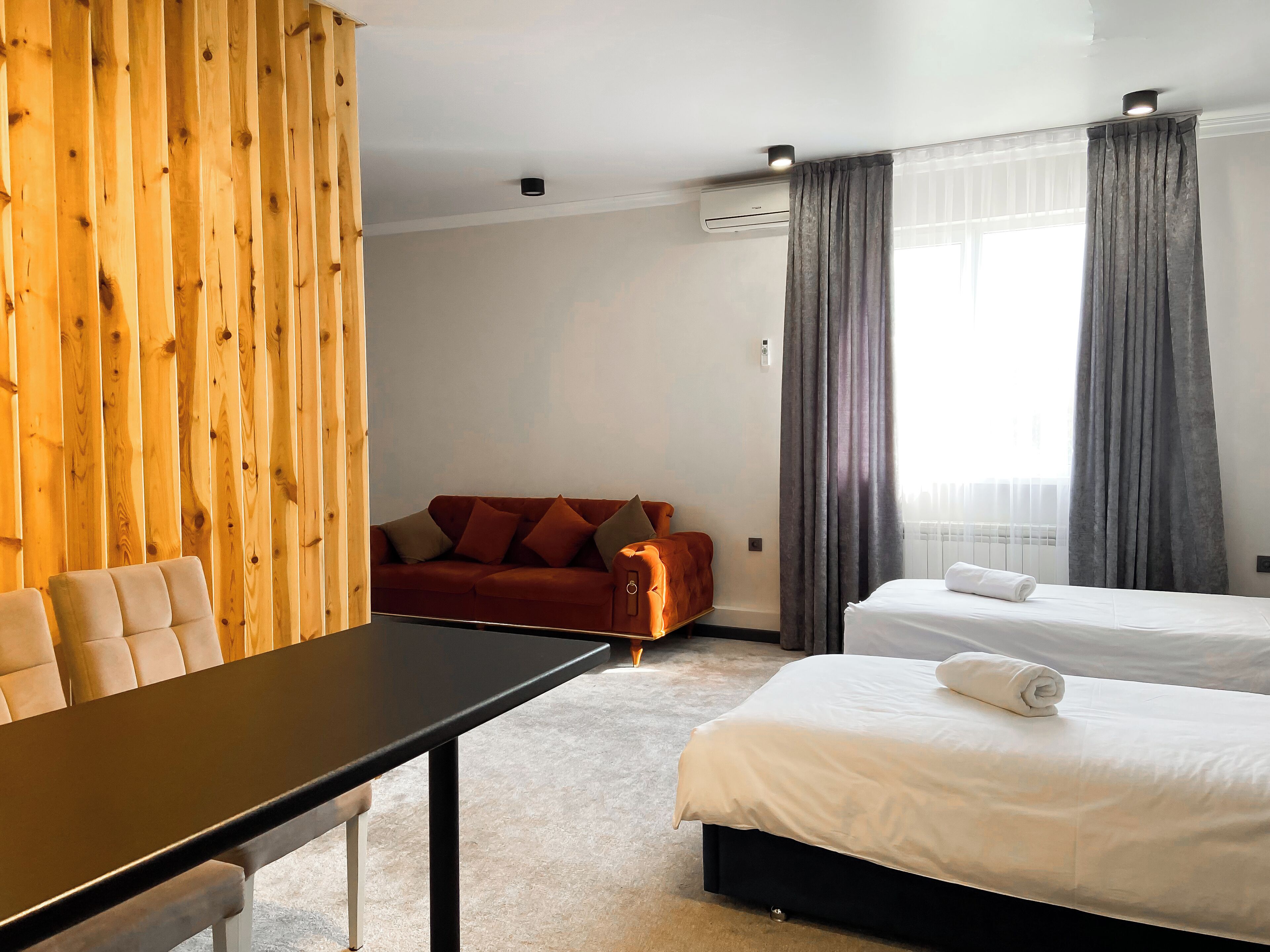 A hotel room with a wooden accent wall, a sofa, a bed with white bedding, and a table.