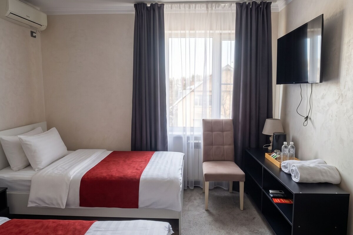 A hotel room with two beds, a desk, a chair, a TV, and a window with curtains.