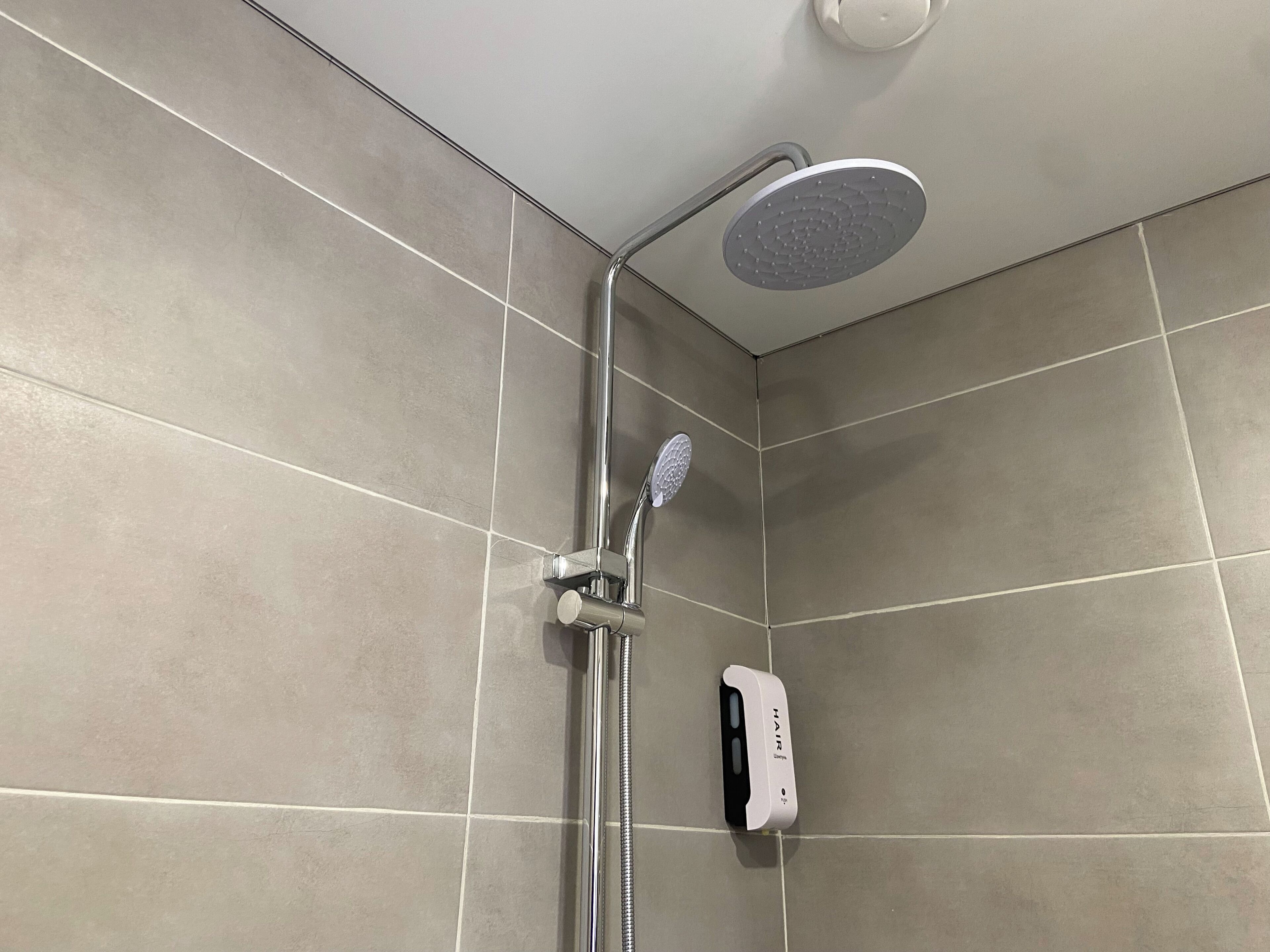 Ducha con cabezal de ducha de mano y panel de control en la pared.