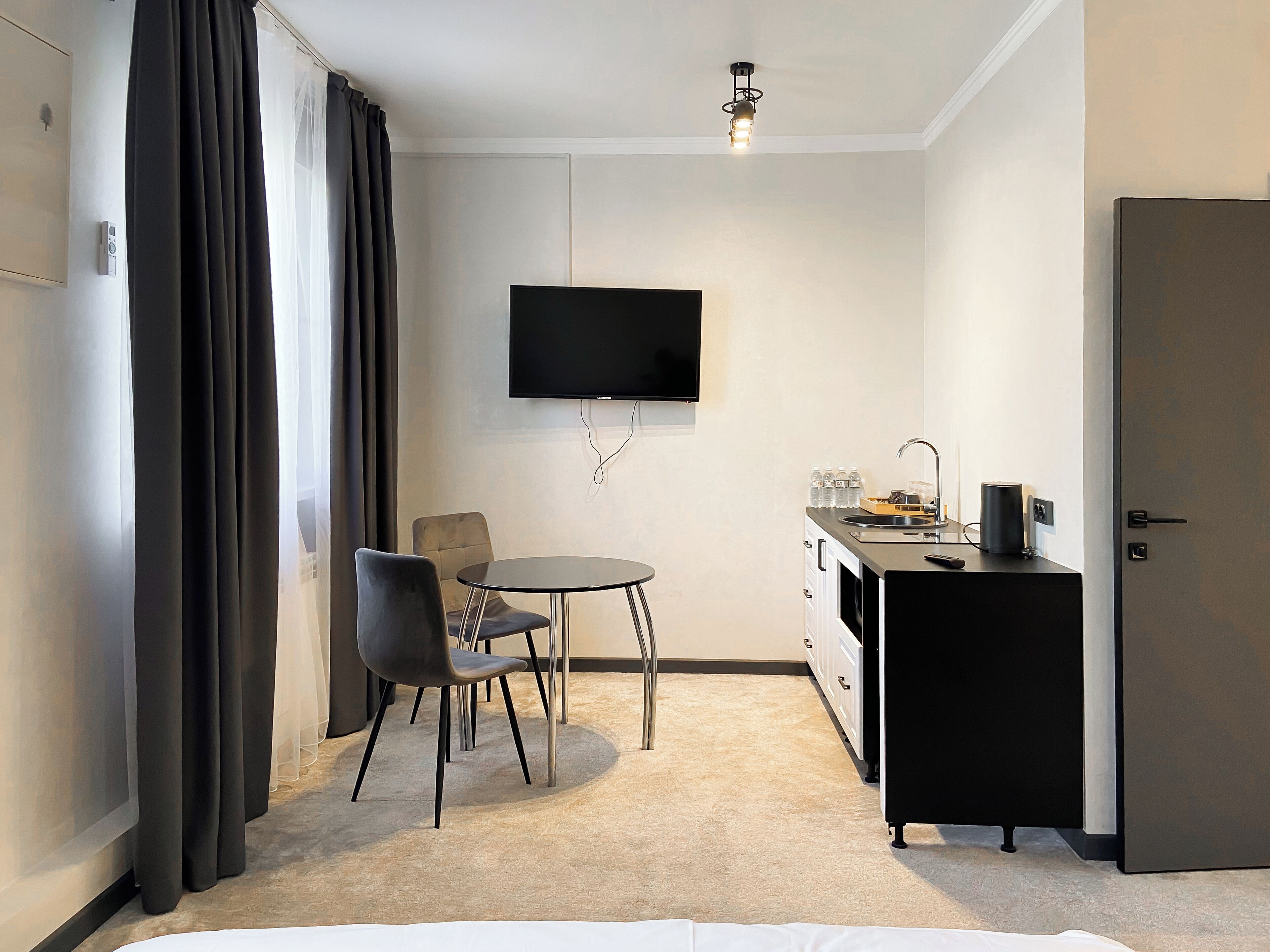 Een compacte hotelkamer met een bed, een klein eettafeltje met twee stoelen, een kitchenette met een spoelbak en kastjes, een flatscreen televisie aan de muur en een deur.