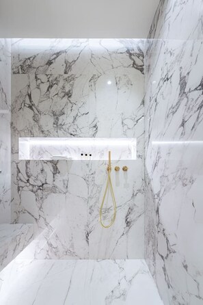 Un baño moderno con paredes de mármol y un grifo de ducha dorado.