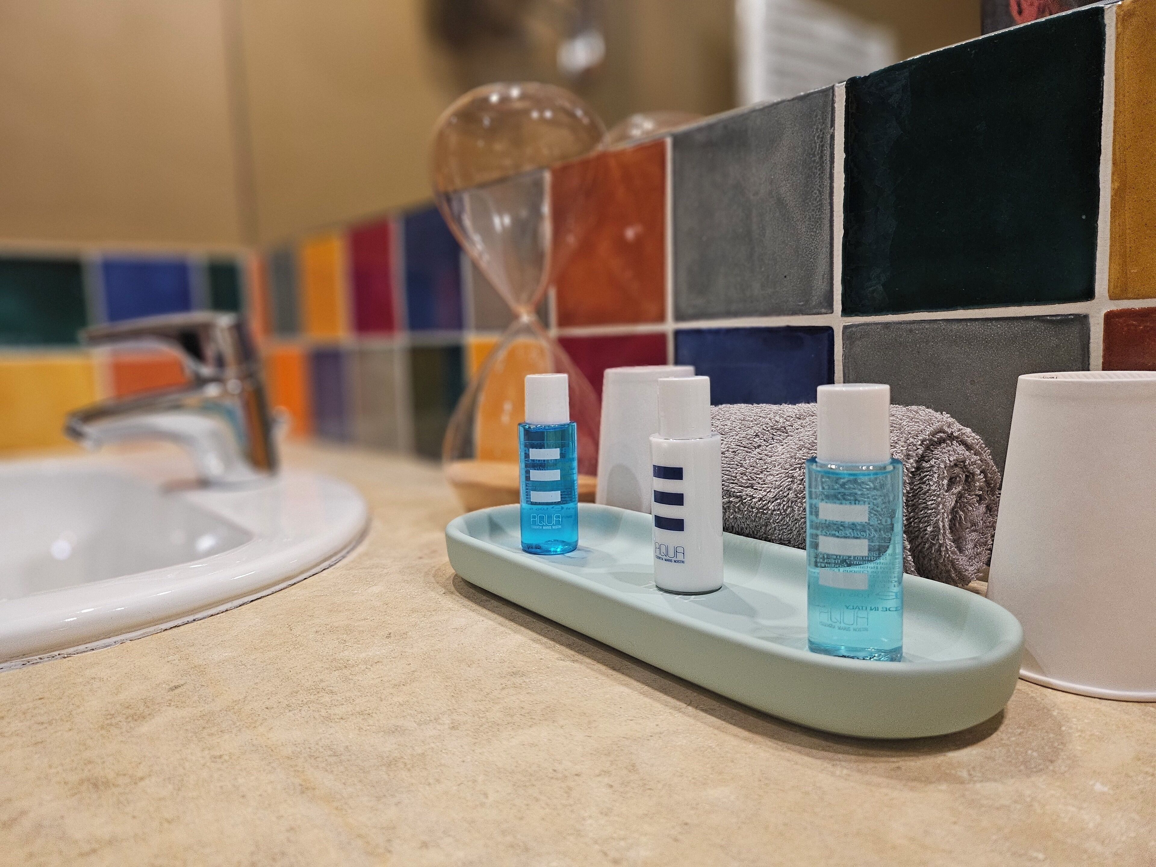 Un baño con un lavamanos, un dispensador de jabón de vidrio y tres botellas de gel antibacterial sobre una bandeja.