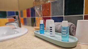 Un baño con un lavamanos, un dispensador de jabón de vidrio y tres botellas de gel antibacterial sobre una bandeja.
