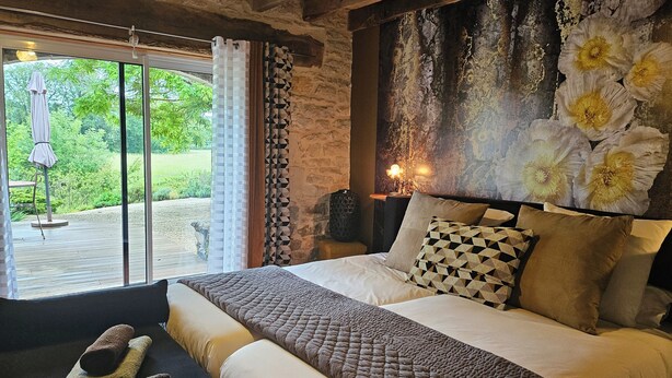 A bedroom with a large bed, a view of the outdoors, and a stone wall. - La Grange Padirac (Padirac)