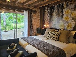 A bedroom with a large bed, a view of the outdoors, and a stone wall. - La Grange Padirac (Padirac)