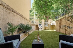 Une cour avec une table, deux chaises, une bouteille de vin et un verre.