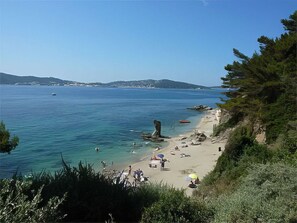 Une plage côtière avec une eau claire, un promontoire rocheux et quelques bateaux.