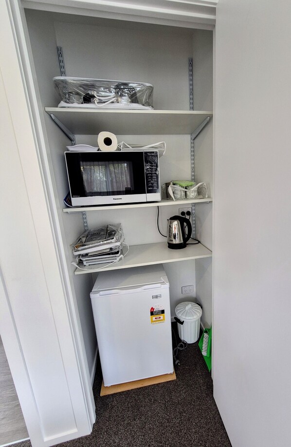 A compact kitchenette with a microwave, kettle, and refrigerator on shelves.