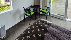 A room with a bed, a TV mounted on the wall, a small table with two chairs, and a window with curtains. - Private Studio - Perfect for short stays in Taupo. (Taupo)