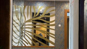 Un intérieur moderne avec une cloison en verre ornée d’un motif de feuilles, un sol carrelé et un mur à motifs.