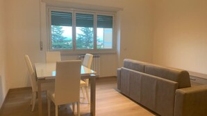 Een kamer met een eettafel en stoelen, een bank en een raam met jaloezieën.