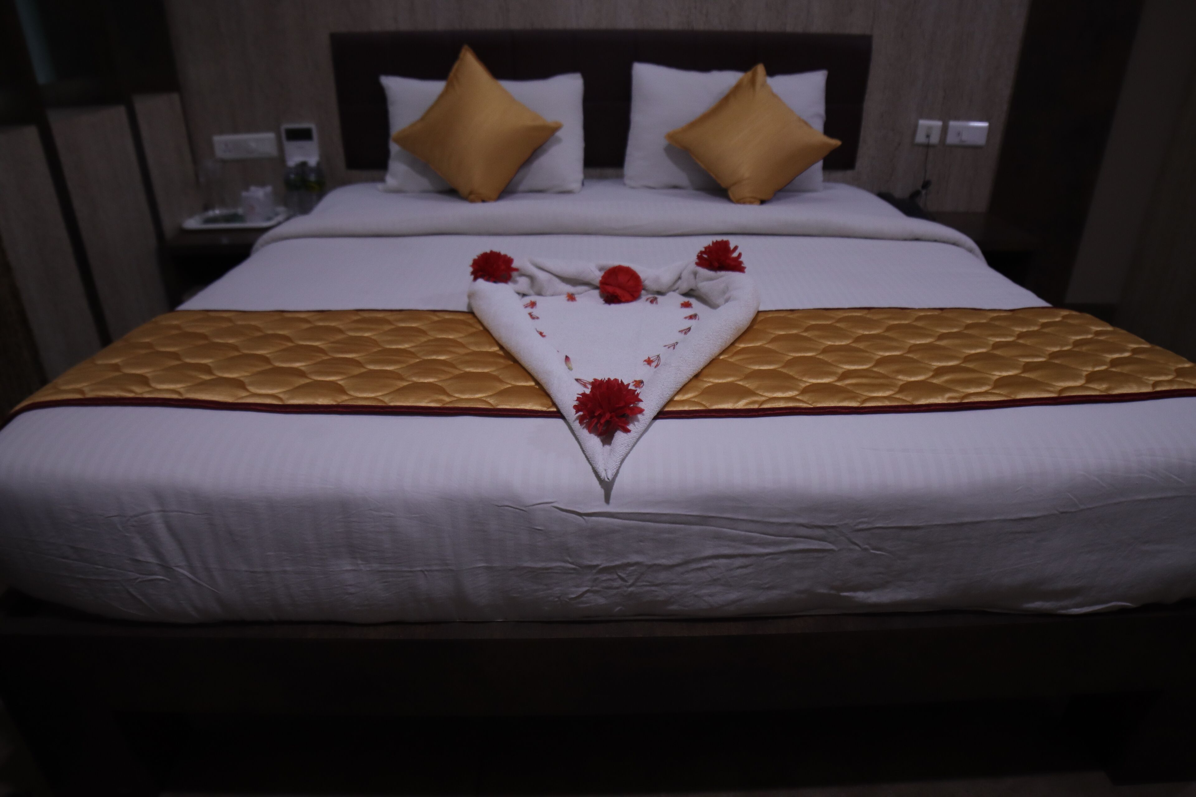 A neatly made bed with a heart-shaped decoration, a wooden headboard, and two gold-colored pillows.