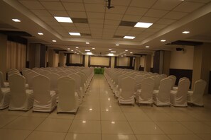 A conference room with rows of chairs, a projector screen, and a stage.
