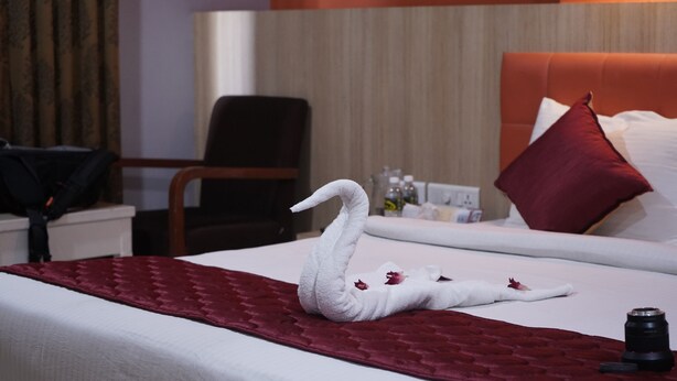 A hotel room with a bed, a red blanket, a swan-shaped towel, and a camera on the bed. - Hotel PL A Residency Tiruchirappalli (Tiruchirappalli)