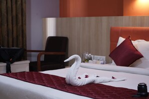 Een hotelkamer met een bed, een rode deken, een handdoek in de vorm van een zwaan en een camera op het bed.