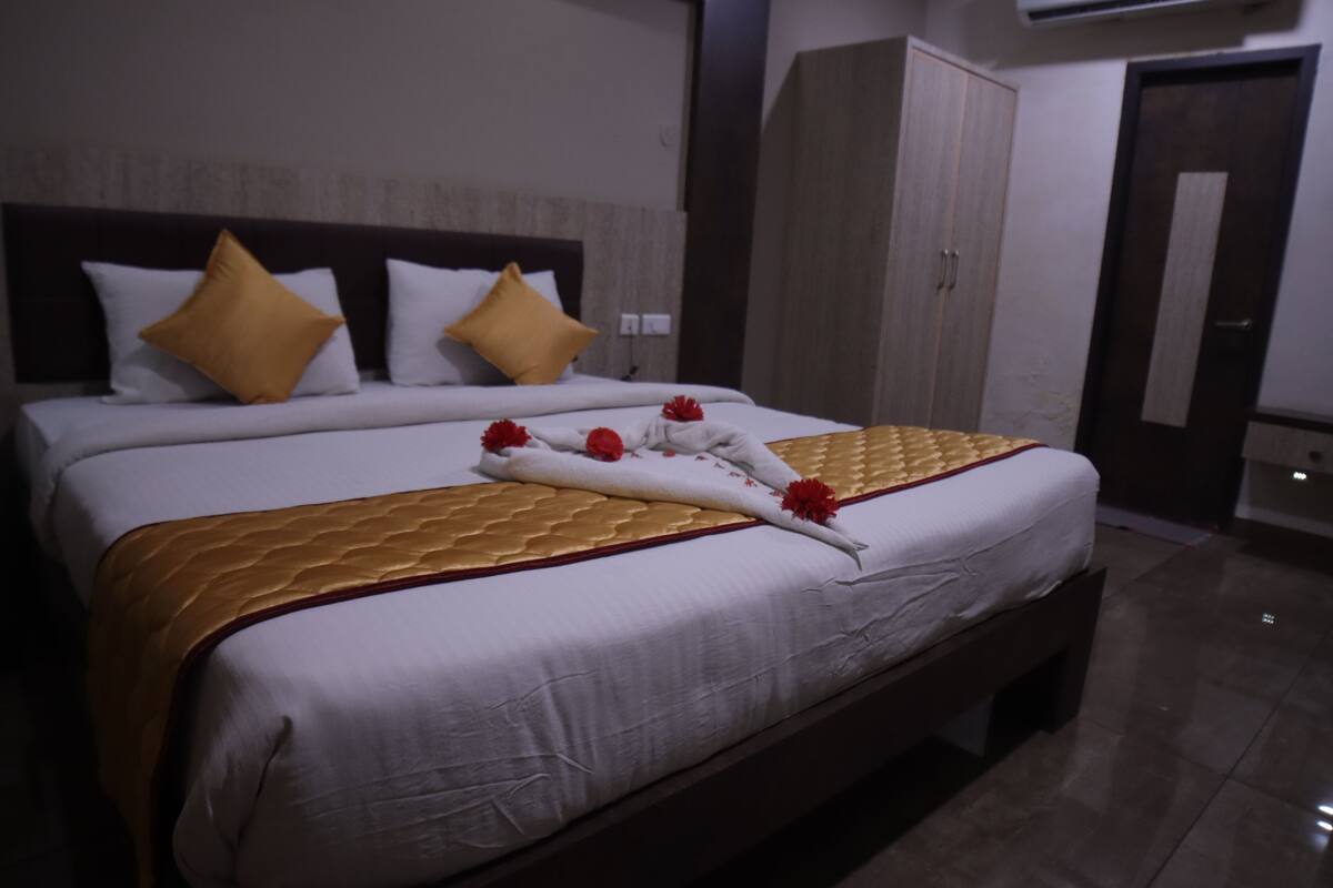 A neatly made bed with a golden quilt, white bedding, and decorative flowers.