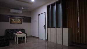 A room with a sofa, a small table with flowers, a door, and a window with curtains. - Hotel PL A Residency Tiruchirappalli (Tiruchirappalli)