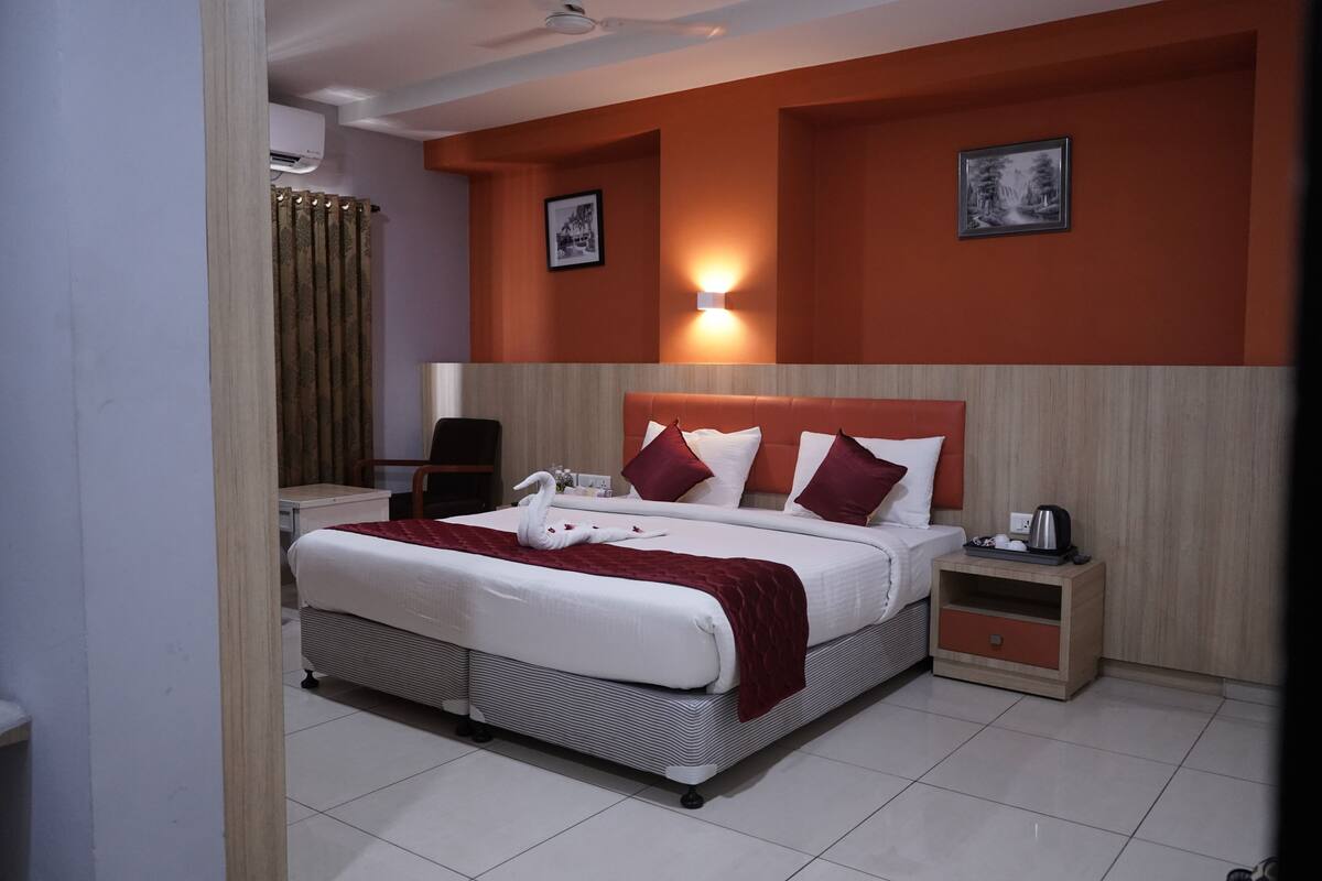 A hotel room with a large bed, a nightstand, a desk, a chair, and a wall-mounted air conditioner.