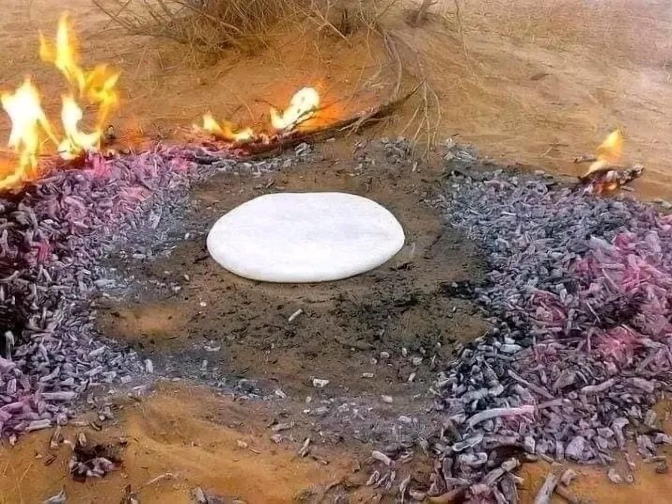 A flatbread cooking over an open fire with wood shavings and embers around it.