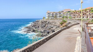 A coastal road with a stone wall, leading to a building with multiple balconies overlooking the ocean. - Balcón del Mar by Interhome (Costa del Silencio)