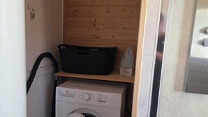 Une petite buanderie comprenant un lave-linge, un étendoir et une étagère avec un panier et un fer à repasser.