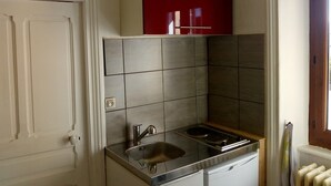 Une cuisine de taille réduite, équipée d’un évier, d’une cuisinière et de meubles de rangement supérieurs de couleur rouge.