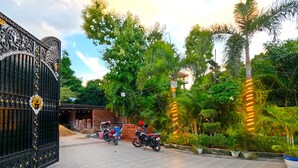 A gated entrance with two motorcycles parked inside, surrounded by lush greenery and potted plants. - THE MANTRA A LUXURY BOUTIQUE HOTEL (Patna)
