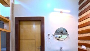 A bathroom with a wooden door, a round mirror, and a white sink on a granite countertop. - THE MANTRA A LUXURY BOUTIQUE HOTEL (Patna)