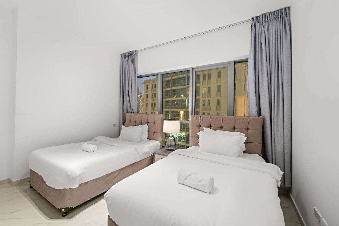 Une chambre d’hôtel avec deux lits, une table de chevet et une fenêtre avec des rideaux.