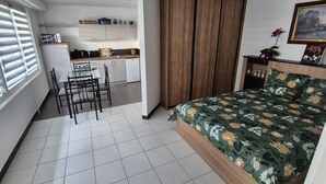 A bedroom with a bed, a dining table with chairs, a kitchenette, and a wardrobe.