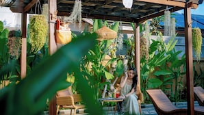 A covered outdoor seating area with wicker furniture, hanging plants, and a table with a drink. - Sapta D'Villa Residence by Purely (Sukawati)