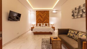 A modern bedroom with a large bed, a sofa, a TV, and a wooden accent wall. - Sapta D'Villa Residence by Purely (Sukawati)