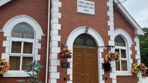 Un edificio de ladrillo rojo con detalles blancos, una puerta de madera y un cartel que indica que es la capilla Capel Newydd de 1930.