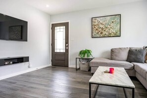 Een moderne woonkamer met een flatscreen televisie, een bank, een salontafel en een deur met een raam.