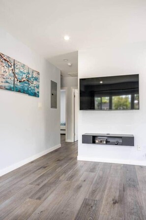 A hallway with a modern design, featuring a wooden floor, a mounted flat-screen TV, and a wall-mounted console.