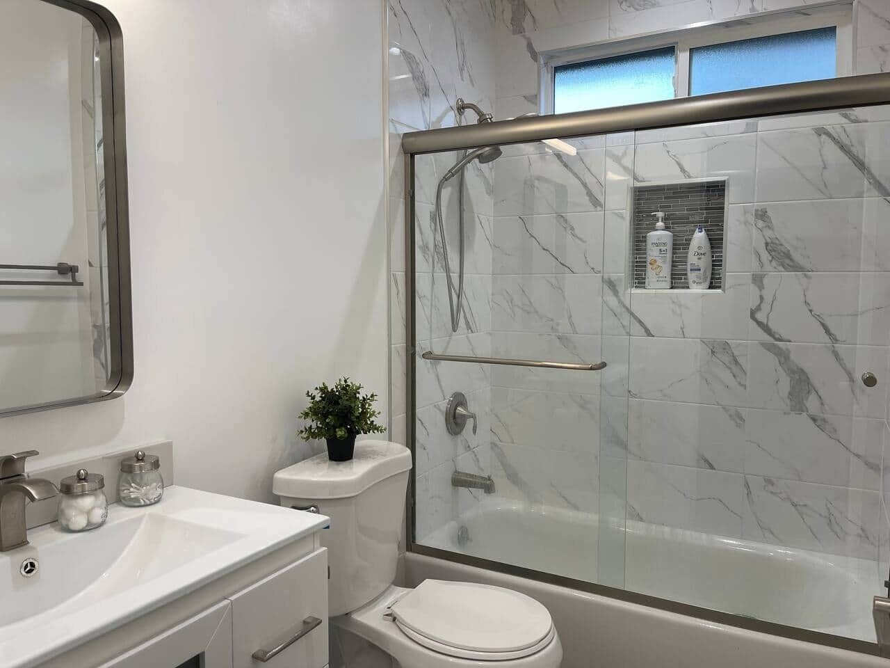 Ein Badezimmer mit Duschkabine, Toilette, Waschbecken mit Spiegel und Pflegeprodukten an der Wand.