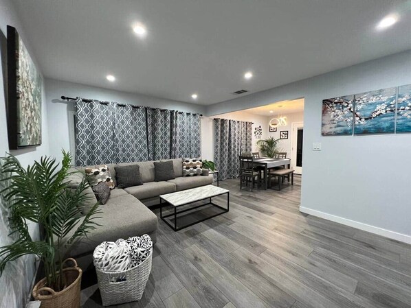 A modern living room with a grey sofa, a coffee table, and a dining area with a table and chairs.