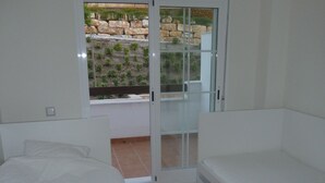 A bedroom with a bed, a bench, and a sliding glass door leading to a balcony with a view of a garden and stone wall. - Magnificent apartment. in luxury complex - swimming pools (AN)